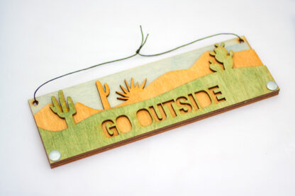 Desert text sign with text "go outside," in green, skewed left