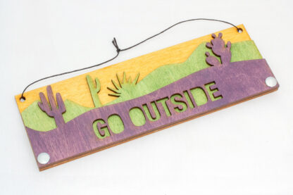 Desert text sign with text "go outside," in purple, skewed left