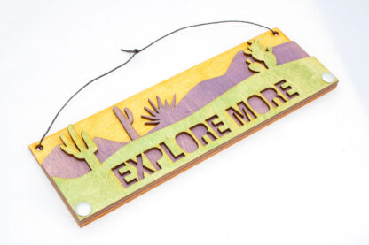 layered desert wooden sign, reads "Explore More," in green, skewed right